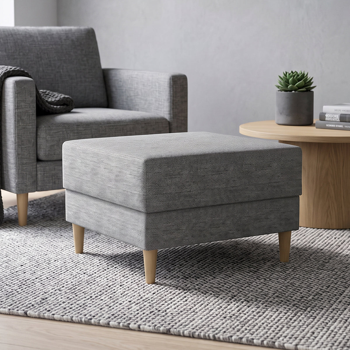 Pouf Harmi 66x66 im Wohnzimmer vor einem grauen Sessel, neben einem runden Tisch mit Sukkulente – Pouf fürs Wohnzimmer