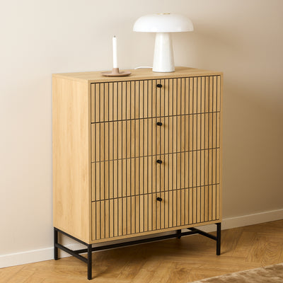 Die Kommode „Bambouz“ (81 x 100) vor einer beigen Wand mit einer weißen Lampe und einer Kerze auf einem Parkettboden im Fischgrätenmuster – eine Kommode für das Schlafzimmer