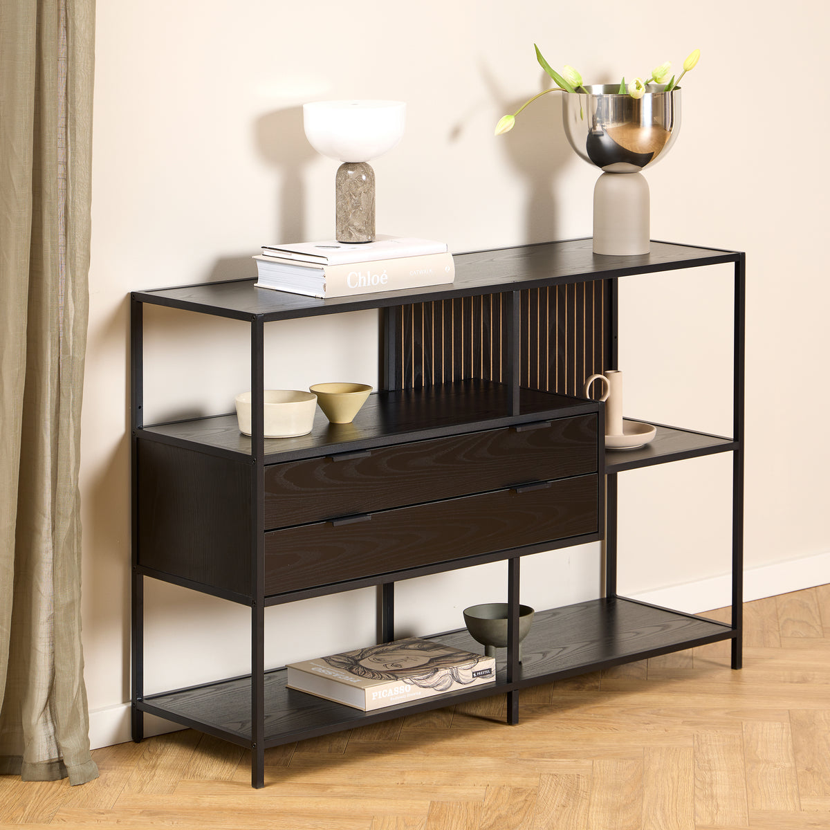Niedriges Regal „Skeleto“ 114 x 78, schwarz melaminbeschichtet, vor einer hellen Wand, mit einer Lampe und einer Vase mit Tulpen auf der Ablage