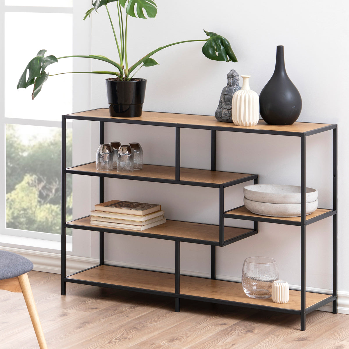 Das Regal „Skeleto“ 114 x 78 in der Ausführung „Wilde Eiche“ in einem hellen Wohnzimmer am Fenster, mit einer Pflanze, Vasen und Büchern – ein Regal für das Wohnzimmer