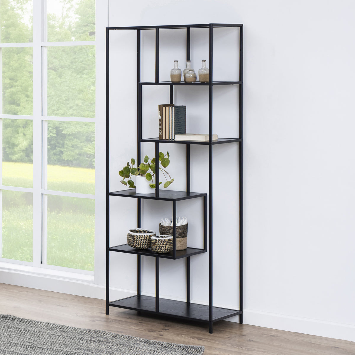Regal „Skeleto“ 77 x 185, schwarze Melaminoberfläche, vor einem großen Fenster mit einer Pflanze, Körben und Büchern – schwarzes Regal für das Wohnzimmer