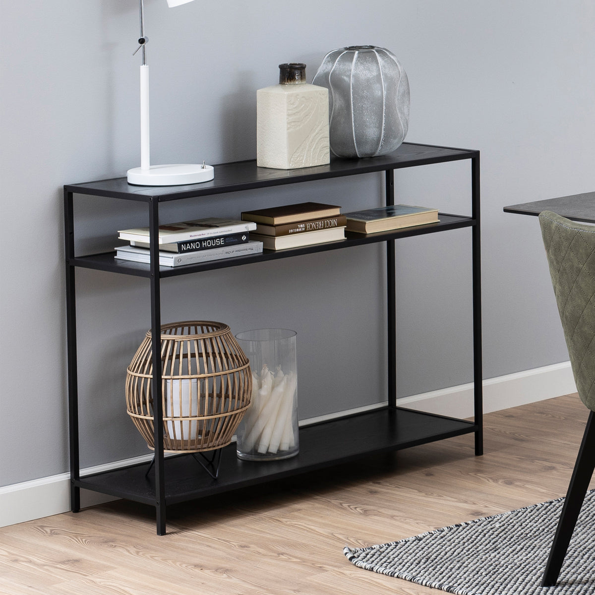 Skeleto-Konsole 100 x 79, schwarz, Melamin, mit Büchern, einer Lampe und einer Laterne auf den Regalen, neben einem Stuhl am Tisch