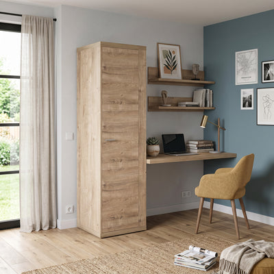 Kleiderschrank Korin 201x57 in hellem Raum mit blauer Wand, neben Regalen und Sessel – schmaler Schrank für kleine Wohnungen