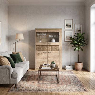 Vitrine Korin 102x160 im Wohnzimmer mit grauem Sofa und Orientteppich – Vitrine fürs Wohnzimmer mit Gläsern